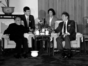 Chinese leader Deng Xiaoping and President Ronald Reagan seated in armchairs. There are two people seated behind them.
